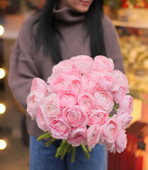 Young woman florist holding big beautiful blossoming mono bouquet of pink ranunculus flowers.