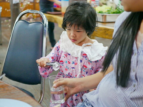A baby girl, 3 years old, learning to serve other family members by serving ice cubes at a dinning table