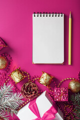 Clean white notepad with pencil around Christmas decorations on pink background. Planning