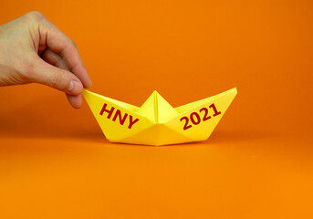 Fototapeta premium 2021 HNY symbol. Image of businessman pushing paper made origami boat forward with words 2021 HNY - Happy New Year. Over orange background with copy space. Business and 2021 HNY concept.