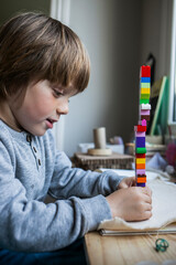 niño alegre y concentrado construyendo torre de piezas de colores en mesa de madera