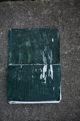 libreta de espiral abierta con hojas pintadas de verde oscuro sobre baldosa de piedra