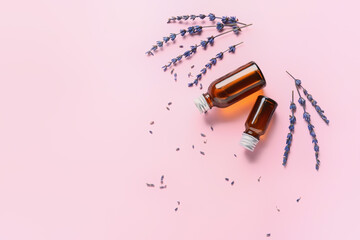 Lavender twigs and bottles with essential oil on color background