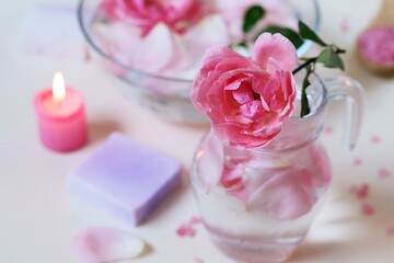 Fresh pink roses, water, petals, candles on a light background, body care products, natural home cosmetics, healthy lifestyle