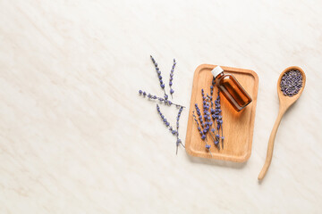 Lavender twigs and bottle with essential oil on light background