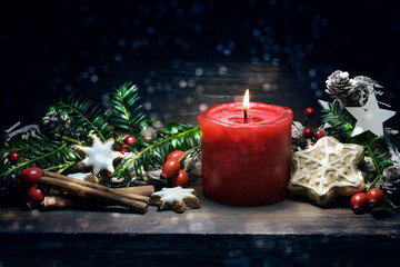 Red burning candle, gingerbread cookies, rose hips, branches and cones as Christmas or Advent decoration on a dark blue wooden background, copy space
