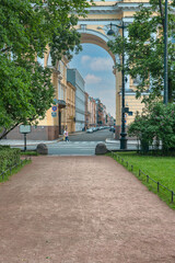 Fototapeta premium the view from the park path through the arch to the stone-paved street with many parked cars against the blue summer sky. St. Petersburg. Russia
