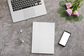 Blank magazine, laptop, mobile phone and flowers on grey background