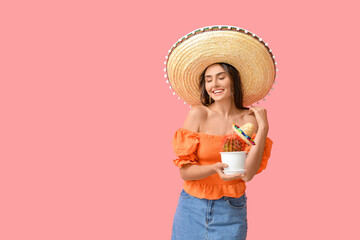 Beautiful young woman in sombrero hat and with cactus on color background