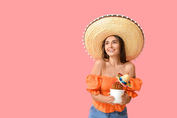 Beautiful young woman in sombrero hat and with cactus on color background