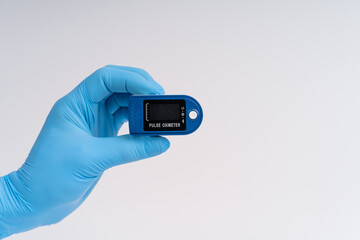 Pulse oximeter on a white background. A hand in a medical glove holds a device for health diagnostics