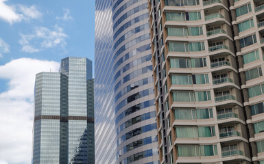 Fototapeta na wymiar Bangkok, Thailand - July 10, 2019 : Angular geometric mirror cladding on a modern building with repeating structure and reflected sky and clouds. No focus, specifically.