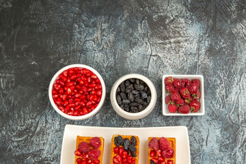 top view waffles with berries on rectangular plate bowls with raspberries raisins pomegranates on grey-white background with copy space