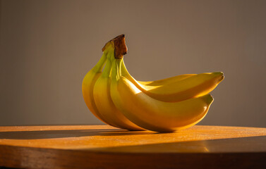 Still life of bananas. Bunch of bananas on a wooden table lit by natural sunlight. Minimal creative design. Dark background,