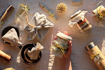 Top view with Zero waste Christmas gifts. Hand holds coffee cup to go. Xmas gift wrapped in towel, bamboo cups, insulated flask. Sustainable presents on neutral natural linen textile.