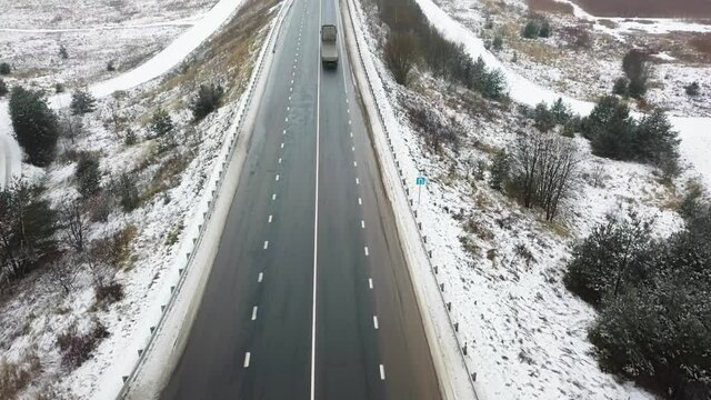 Top view of highway or road, truck and cars driving on snowy road and forest in winter time. The concept of delivery.