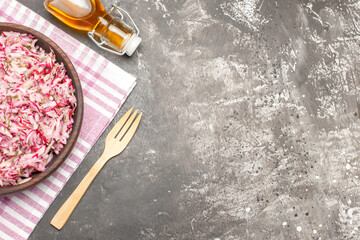 Half shot of delicious vegetable salad on half-folded pink stripped towel on the right side oil bottle and fork on dark table