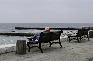 Naklejka na ściany i meble The girl is sitting on a bench by the sea. The girl is resting by the sea.