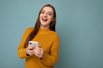 Laughing attractive positive good looking young woman wearing casual stylish outfit poising isolated on background with empty space holding in hand and using mobile phone messaging sms looking at