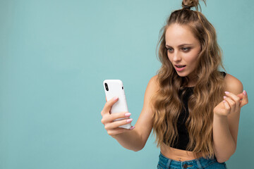 Beautiful young woman wearing casual clothes standing isolated over background surfing on the internet via phone looking at mobile screen