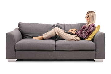 Young woman working on a laptop and laying on a sofa