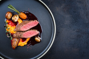 Modern style traditional wild hare back filet braised with wild berries and red wine jus with mashed carrot puree and sweet potato served as top view on Nordic design plate with copy space right