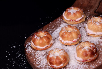 Small home baked cakes, filled with strawberry cream, sprinkled with coconut flour on a dark wooden board and black background