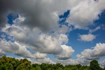 Clouds on blue sky and deciduous forest and meadow.