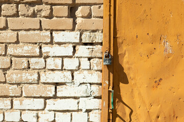 Plain iron lock on an old orange door. Brick wall background