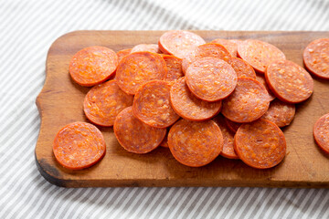 Italian Pepperoni Slices on a rustic wooden board on cloth, side view.