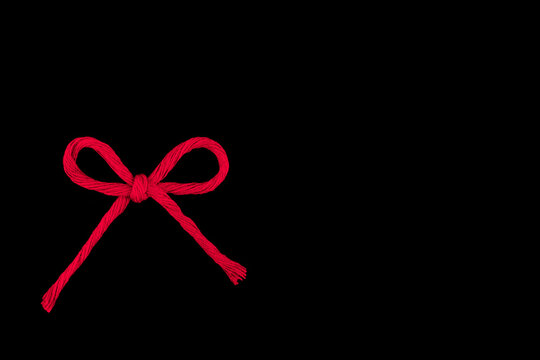 A bow of bright red cotton threads on a black background.Copy space.Selective focus.Concept of decoration,design of packages,cards.