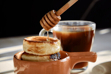 honey is poured on cheesecakes in a brown clay cup, black coffee in a glass