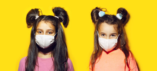 Studio portrait of two teenage girls wearing medical mask on yellow background. Prevention of coronavirus and covid-19. Panoramic photo.