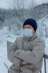 Fototapeta na wymiar portrait of an elderly man in a blue knitted hat in a medical mask and a white jacket in a winter Park.