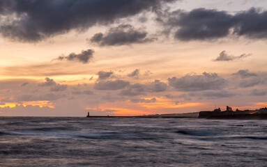 Fototapeta na wymiar Sunrise at a chilly Cullercoats Bay in the north east of England, with Tynemouth Pier and the lighthouse in the distance