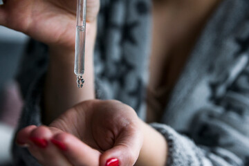A female doctor-cosmetologist in a bathrobe
 holds a bottle of enriched argan oil. Woman with a pipette. Face care product