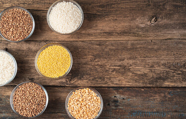 Cereals of different types in round bowls on a wooden background. Top view, with space to copy. Concept of products, culinary backgrounds.