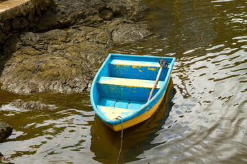 Little blue and yellow row boat sitting abandoned on the shore of a river