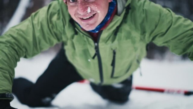 Cross country skier falls in the forest. Young man lies on the snow after falling, looks at the camera and stands up