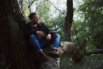 Portrait of a smoking young bearded man adventurer relaxing in the autumn forest and holding a cigarette