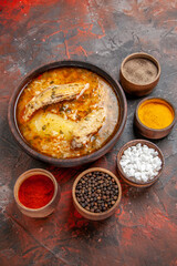 bottom view bowl of chicken soup around different spices on dark red background