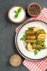 top view stuffed grape leaves on white plate bowls of natural yogurt and black pepper on dark background