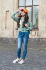 Stylish little girl fix cap with fashion look wearing casual clothes on urban outdoors, style