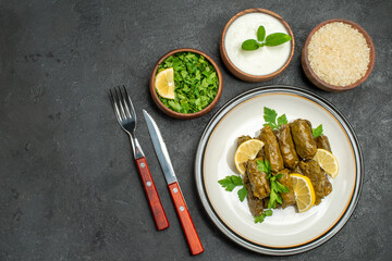 top view stuffed grape leaves on white plate bowl of parsley natural yogurt rice knife and fork on dark backgroundwith copy space