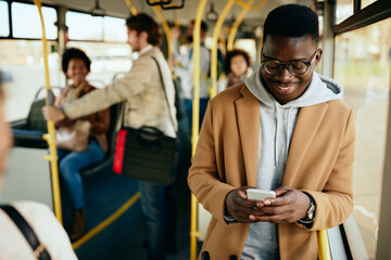 Happy African American man texting on mobile phone while commuting by bus.