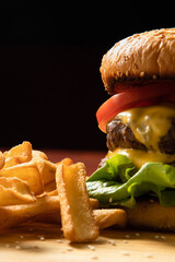close-up of a burger with cheese, cutlets, lettuce, tomatoes and a bun, next to it there are fries, a black background in the bar.