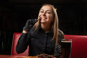 a satisfied girl is eating snacks, a model is holding a jerky in black gloves, a beer is on the table, dinner is in a pub.