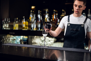 a young bartender pours champagne into a glass from a bottle on the bar.