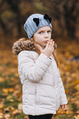 A funny little girl in a jacket of preschool age indulges, smokes a cigarette, imitating adults. Autumn portrait, photography.