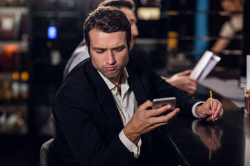 a young man reads a message on his phone, sits in a bar.
